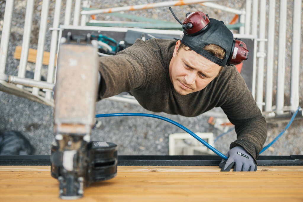 Mies rakennustelineillä naulapyssyn kanssa.