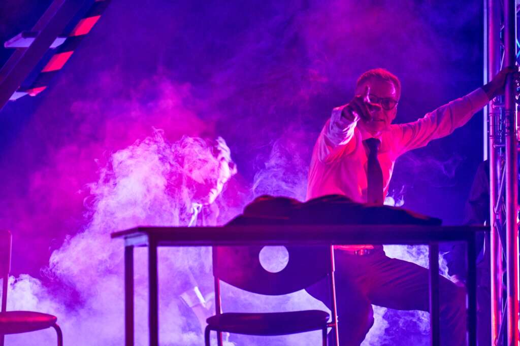 Henkilö seisoo lavalla ja osoittaa eteenpäin, ympärillä savua, kuvituskuva Nokia-näytelmästä.