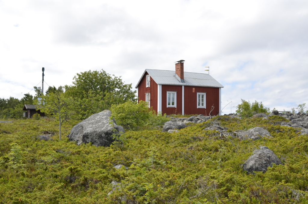 Ett litet rött hus i skärgårdsmiljö